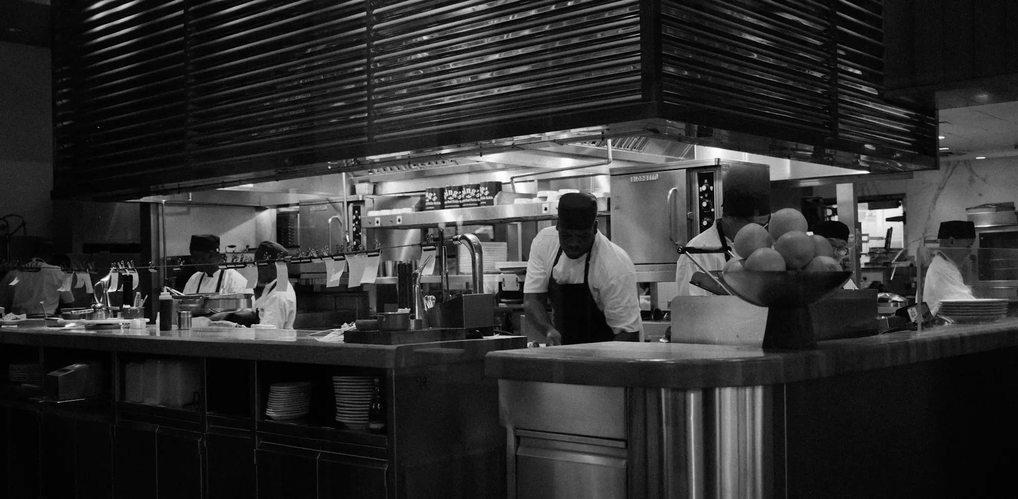 Chefs working at the pass of a busy commercial kitchen with extraction hood overhead