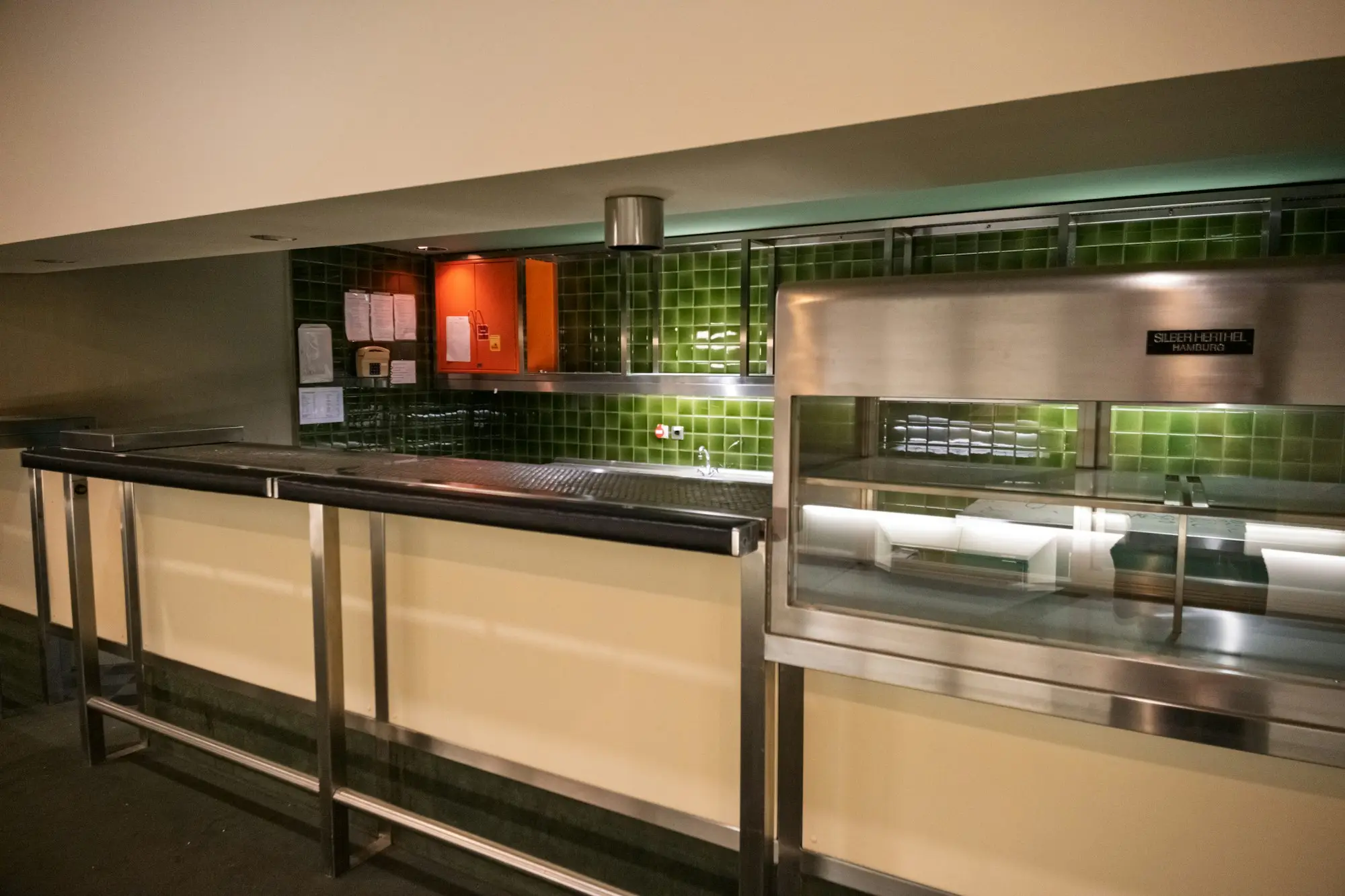 Empty stainless steel serving counter with green tiled splashback in a commercial café kitchen, ready for equipment to be installed