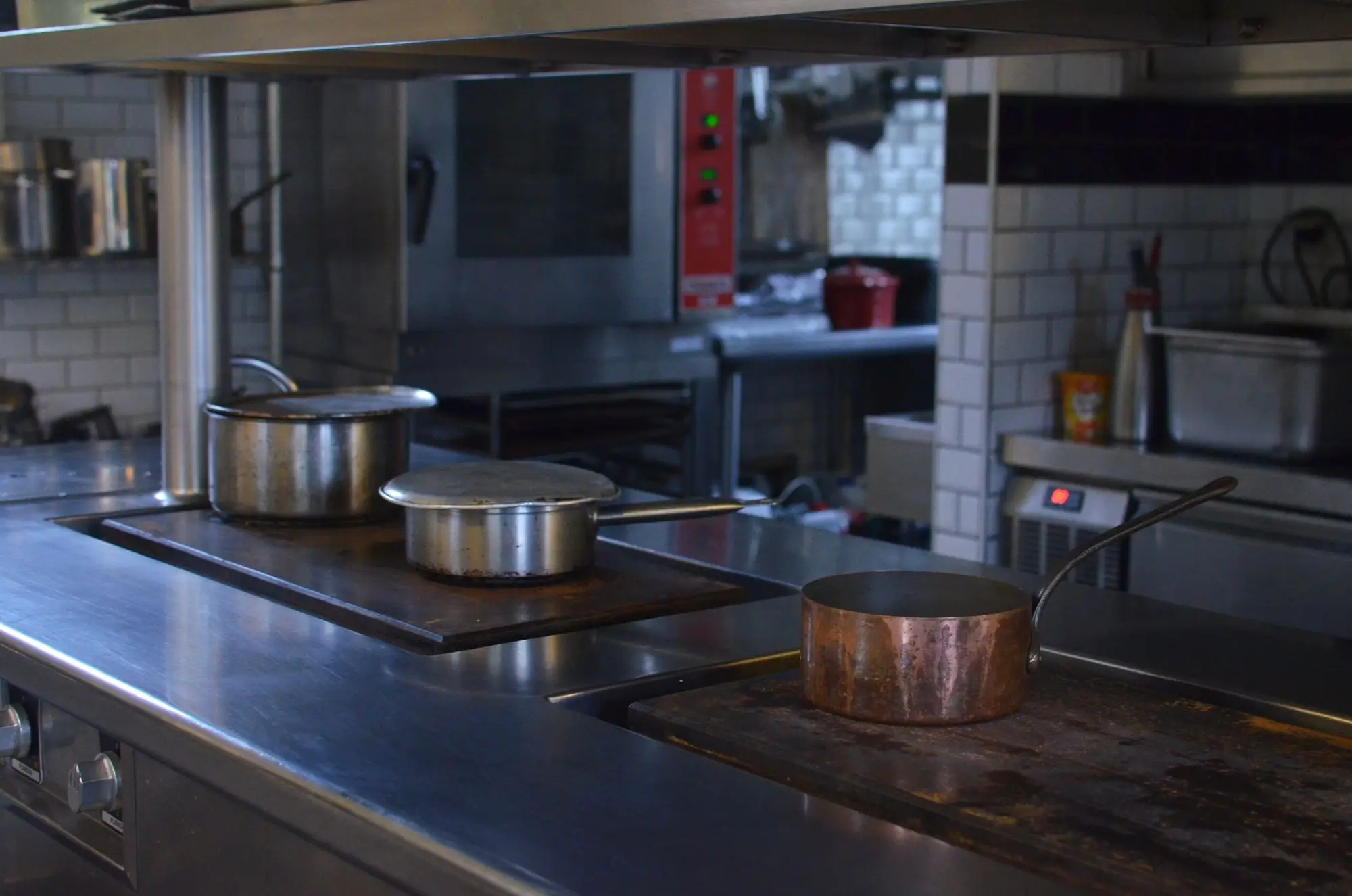 Restaurant kitchen range with stainless and copper pans in front of a combi oven and tiled walls